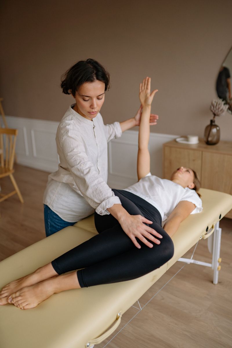 Physiotherapist aids woman with therapeutic exercises indoors.